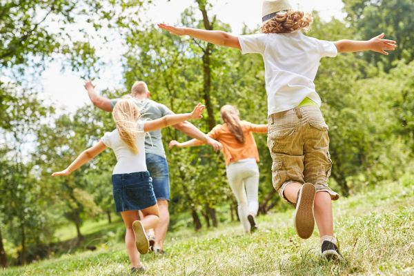 Mann, Frau und zwei Kinder bewegen sich im freien, sie strecken arme weit aus und sind alle von hinten zu sehen.