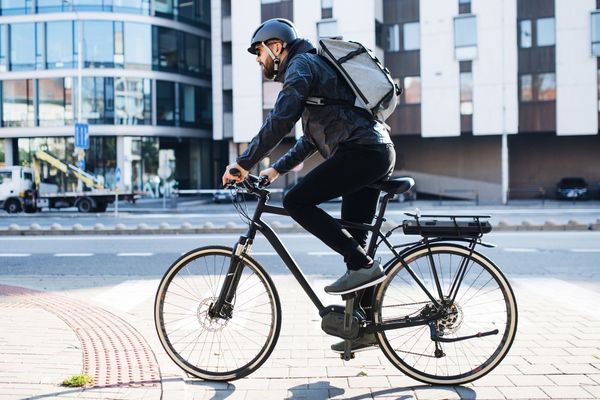 Person mit Fahrradhelm und Rucksack fährt auf einem E-Bike durch eine Stadtstraße.