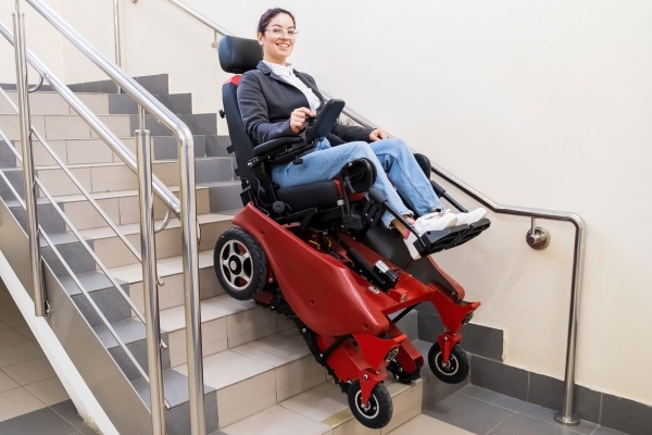 Frau fährt mit einem elektrischen treppensteigenden Rollstuhl eine Treppe mit Metallgeländer hinunter.