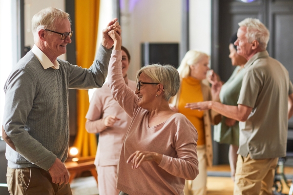 Älteres Paar tanzt gemeinsam in einer Gruppe mit weiteren Seniorinnen und Senioren.