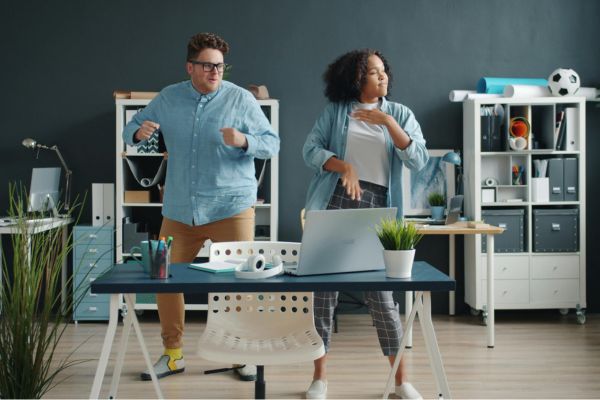 Zwei Personen bewegen sich im Büro neben einem Schreibtisch und machen eine aktive Pause während der Arbeit.