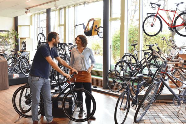 Mann und Frau stehen in einem Fachgeschäft für Fahrräder und unterhalten sich. Der Mann hat das Lenkrad eines Rads in der Hand.