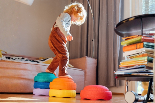 Kind balanciert auf gestapelten Trittsteinen im Wohnzimmer und bewegt sich spielerisch.