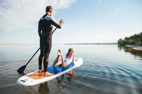 Mann und Frau fahren gemeinsam auf einem Stand-up-Paddle-Board auf ruhigem Wasser.