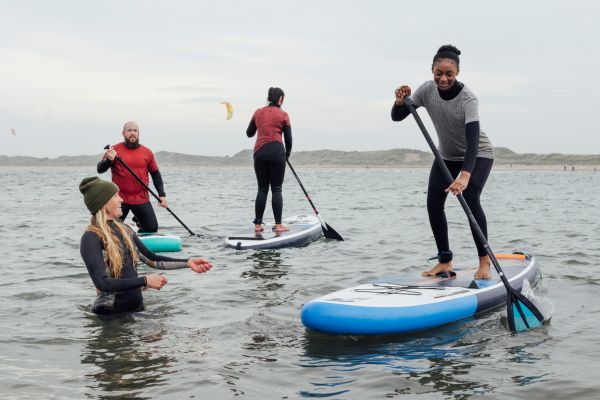 Mehrere Personen stehen auf Stand-up-Paddle-Boards im flachen Wasser und paddeln gemeinsam auf einem See.