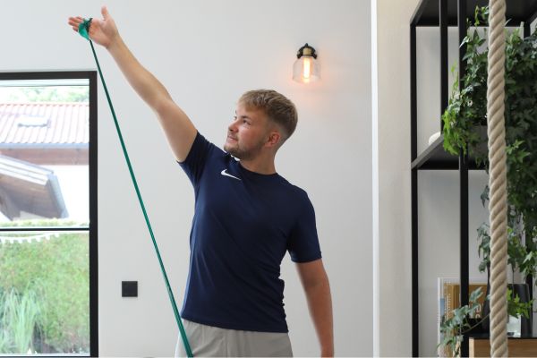 Bild zeigt einen Mann der in einem Zimmer Übungen mit dem Theraband macht. Link führt zu einer Seite mit Rückenübungen mit Theraband