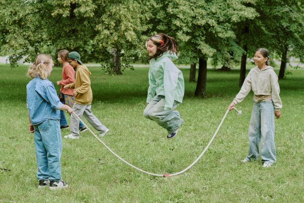 Mehrere Kinder springen gemeinsam Seil und spielen auf einer Wiese im Park.