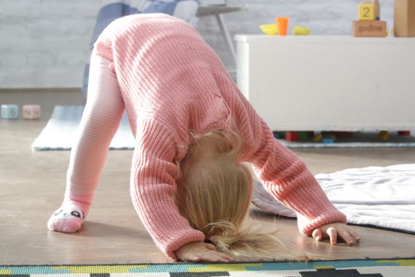 Kleinkind macht eine Vorbeugeübung auf dem Boden und stützt sich mit Händen und Füßen ab.