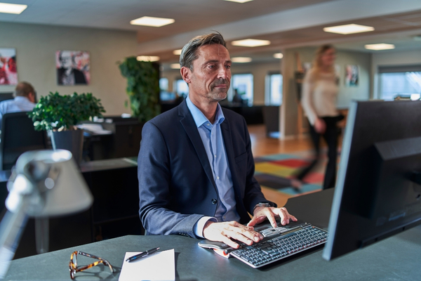 Mann arbeitet im Büro an einem Computer und bedient die Tastatur vor dem Bildschirm.