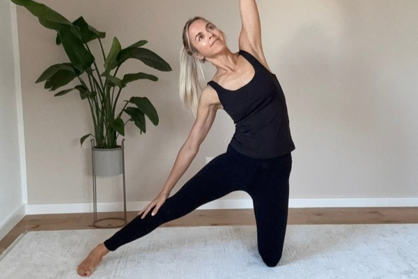 Frau führt auf einer Matte die Yoga-Übung Tor mit seitlicher Oberkörperneigung, ausgestrecktem Bein und erhobenem Arm aus.