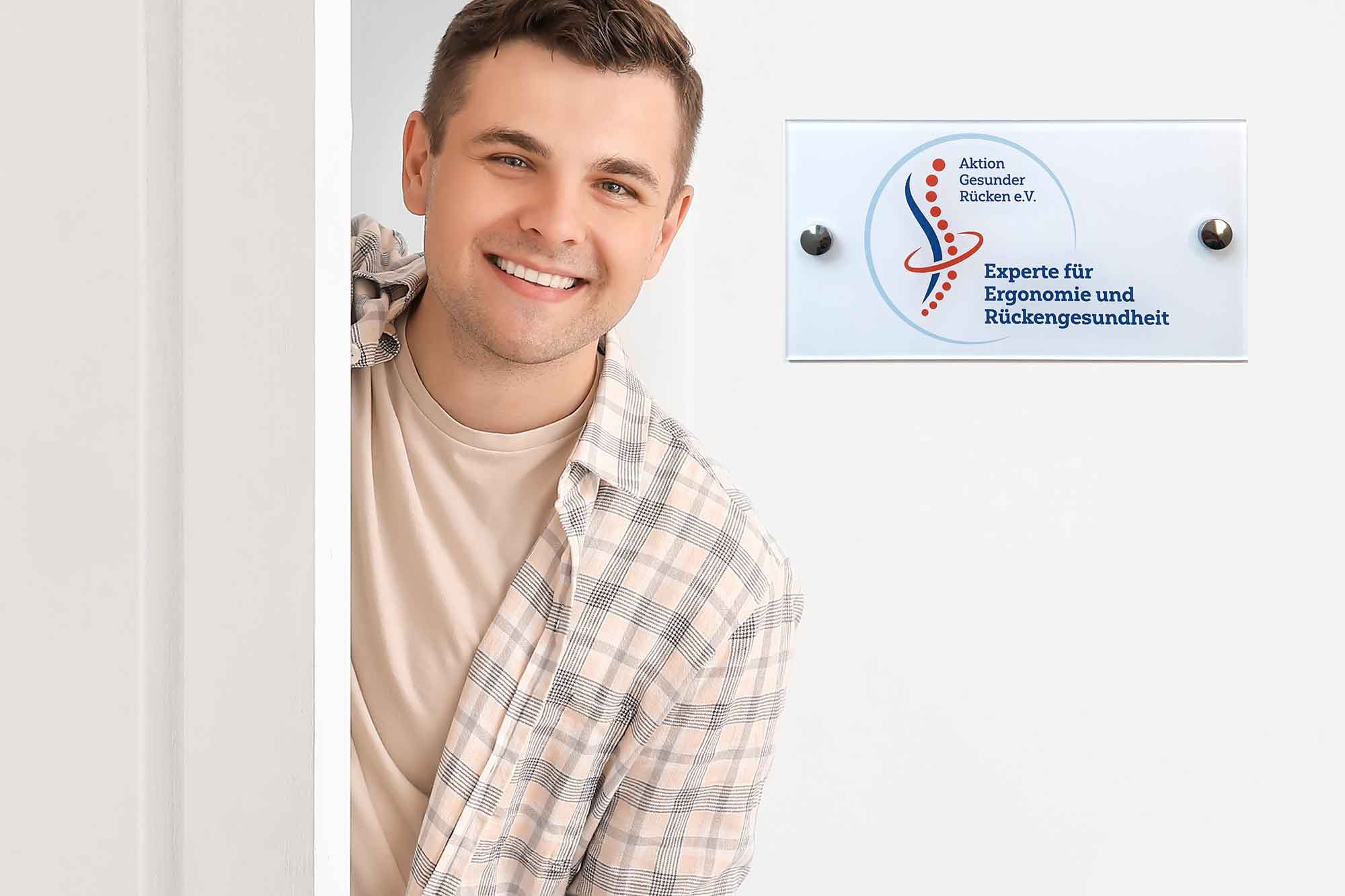 Experte für Ergonomie und Rückengesundheit neben Türschild mit Zertifikat