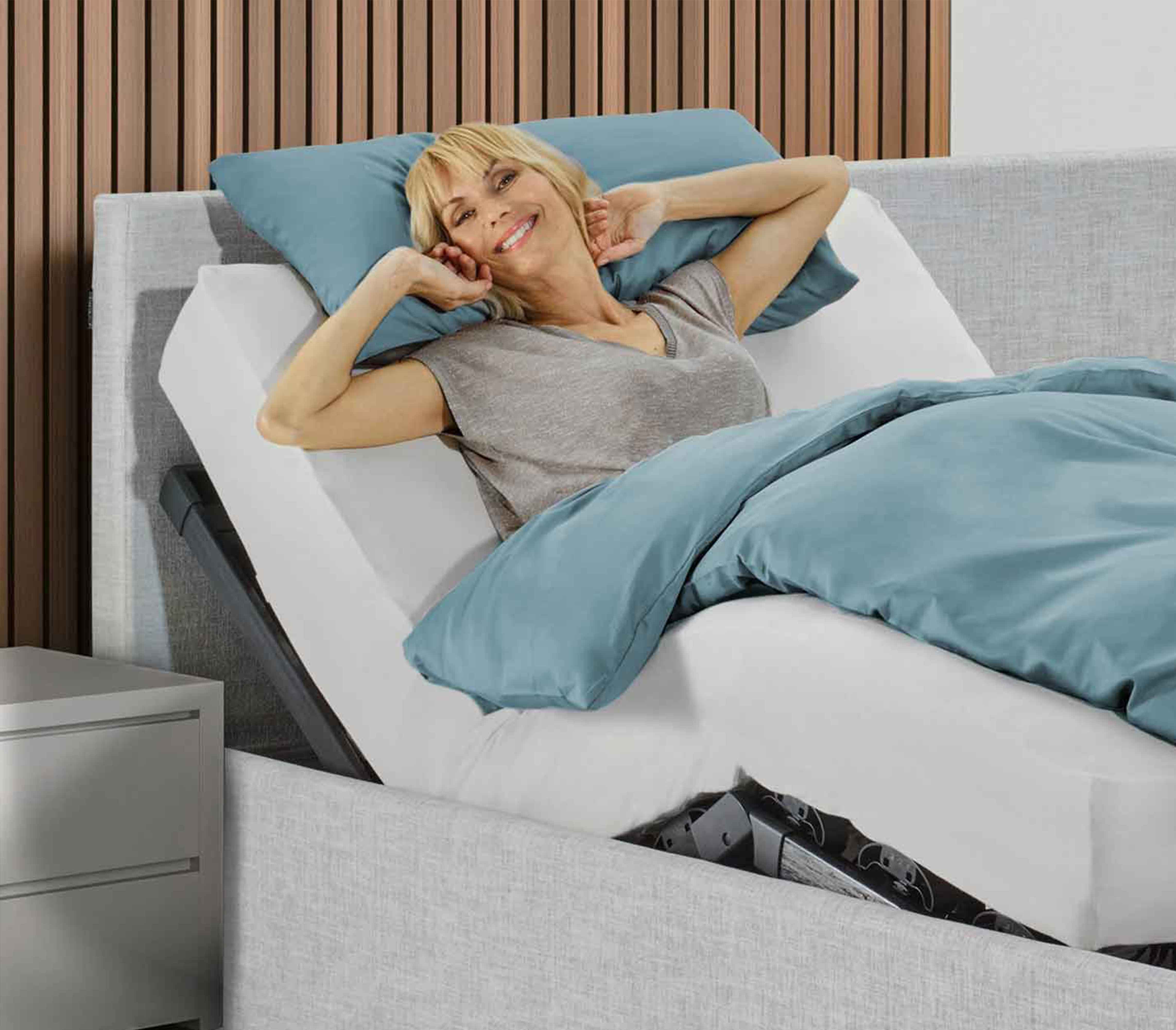 Frau liegt entspannt auf einem verstellbaren Bett mit erhöhtem Oberkörper in einem Schlafzimmer.