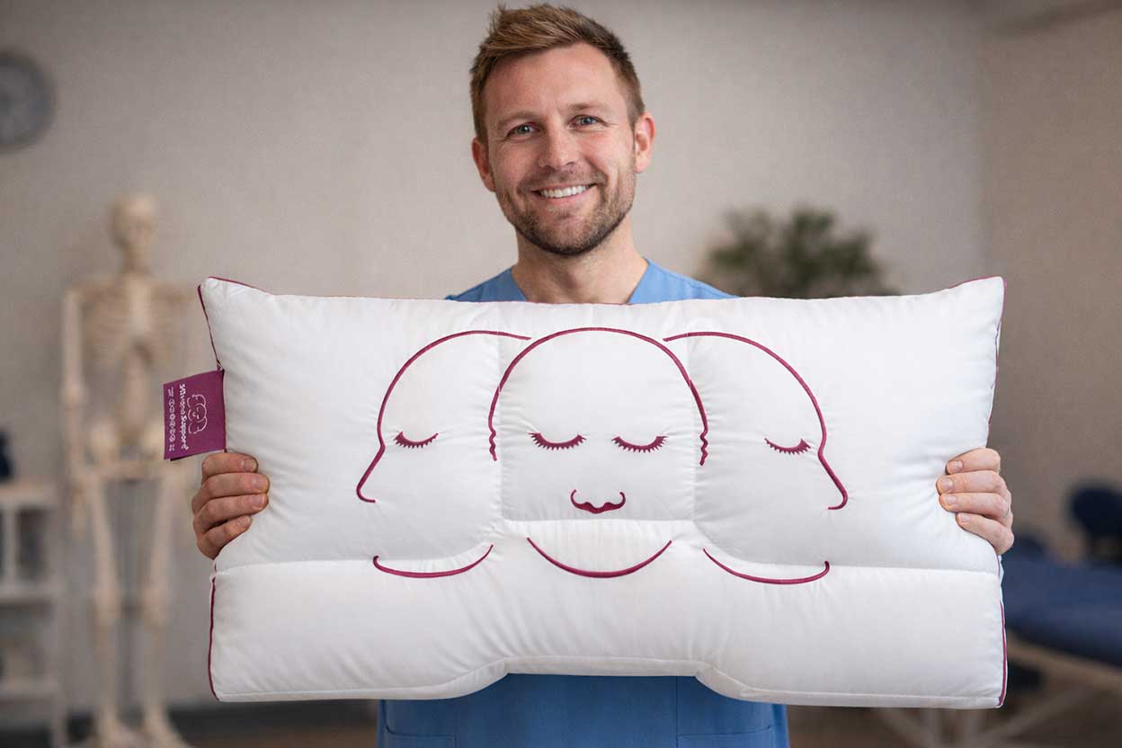 Mann hält ein großes Kopfkissen mit aufgestickten Schlafpositionen vor sich.