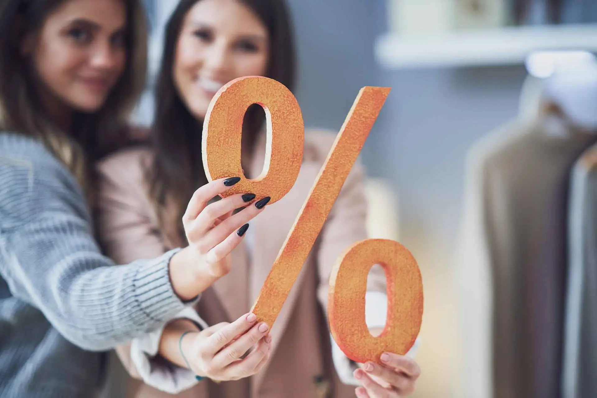 Zwei junge Frauen halten ein großes Prozentzeichen aus Holz in die Kamera.