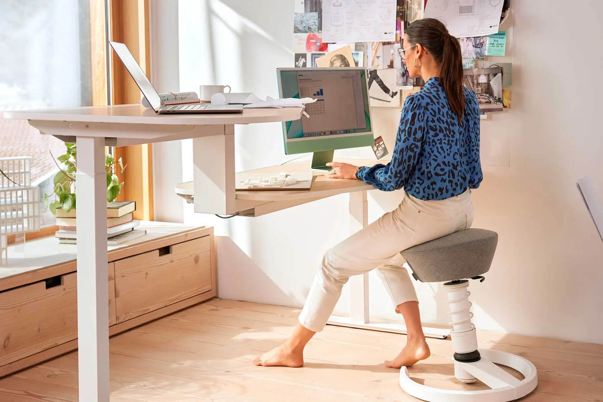 Eine Frau sitzt auf einem ergonomischen Hocker an einem Schreibtisch am Computer.