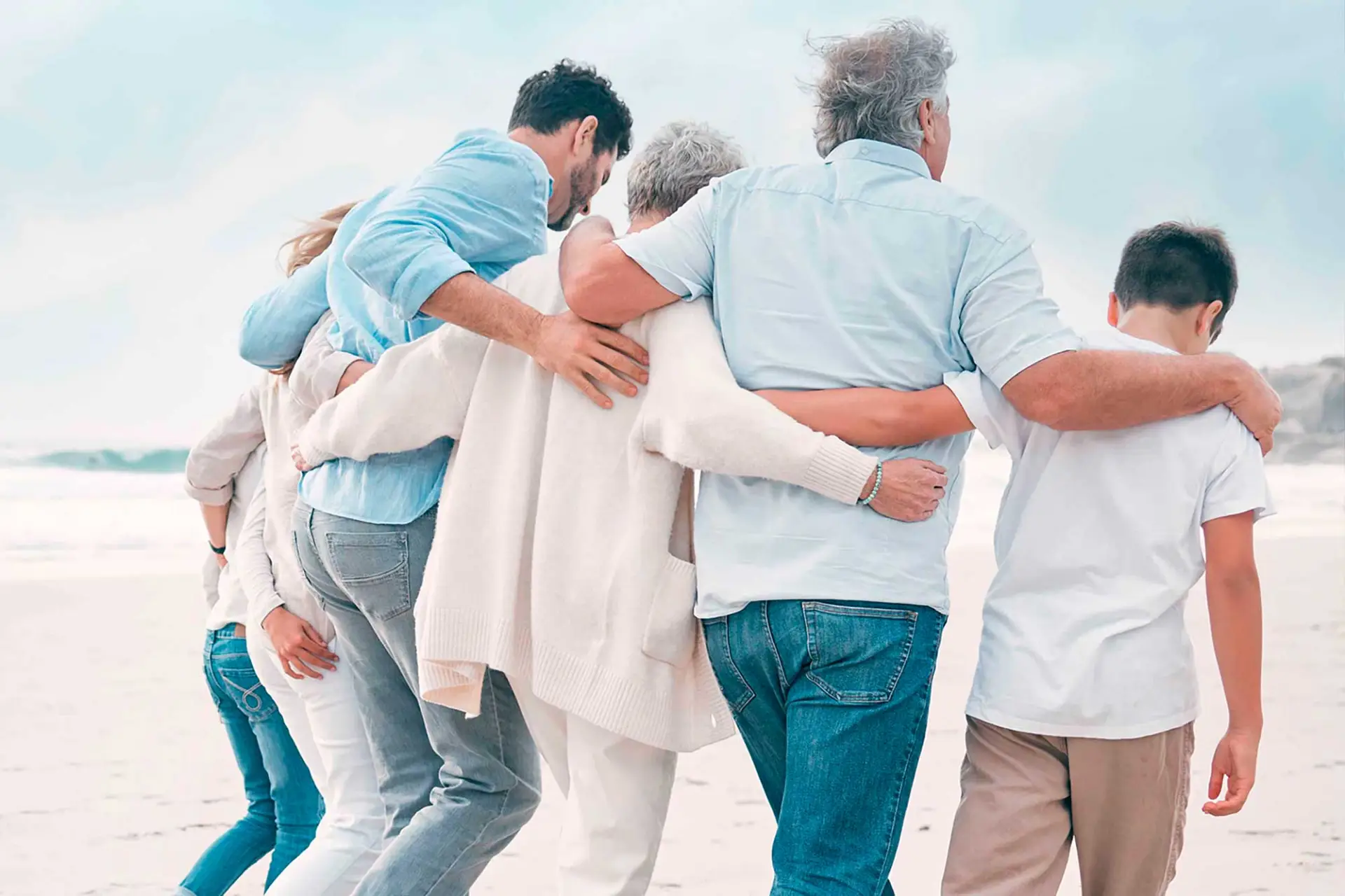 Familie verschiedener Generationen geht gemeinsam am Strand und hält sich gegenseitig fest