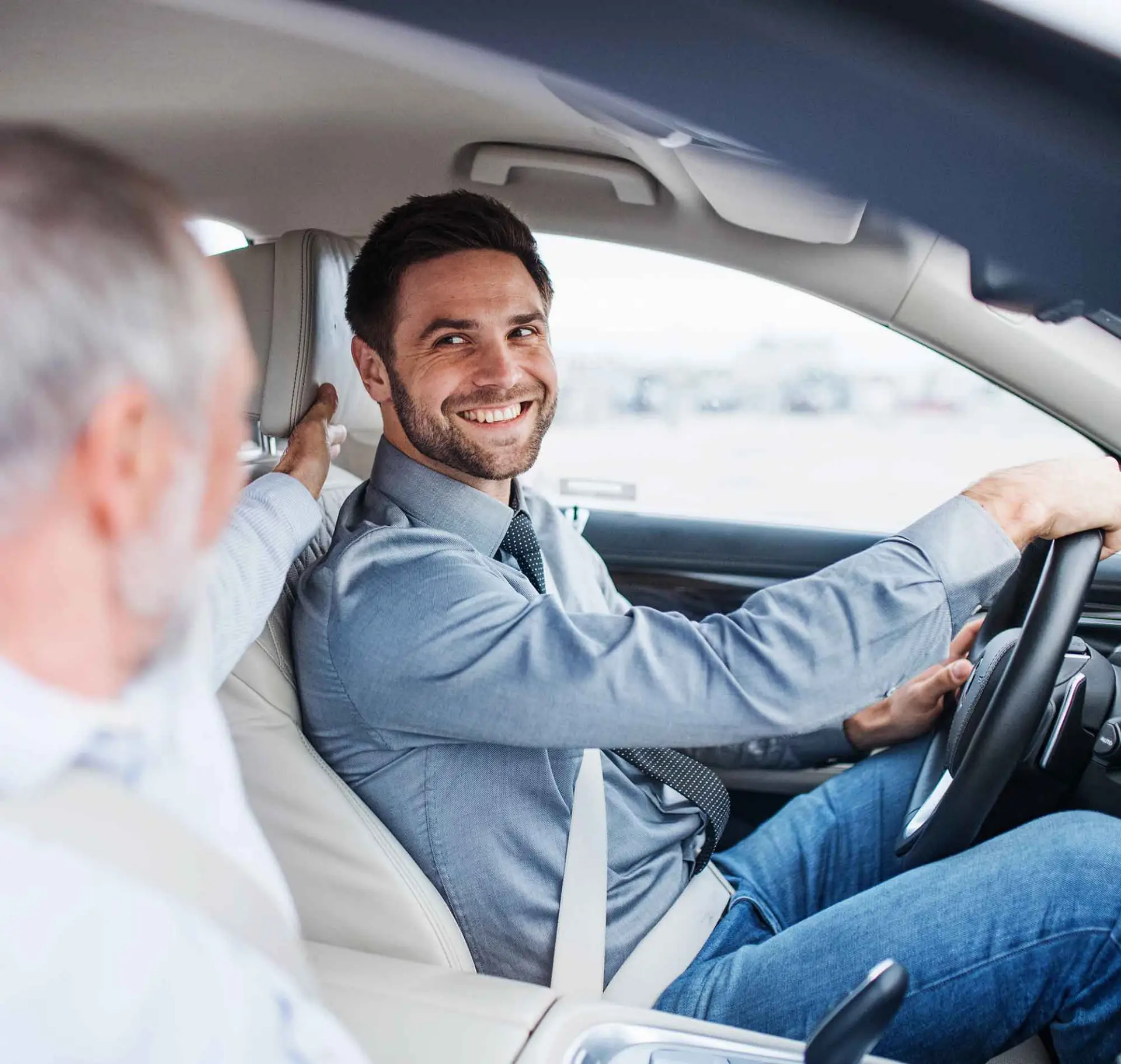 Ein Mann sitzt am Steuer eines Autos und lächelt einen anderen Mann auf dem Beifahrersitz an.