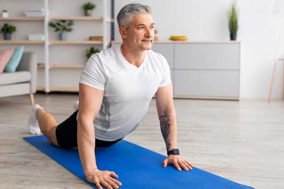 Ein Mann dehnt den Rücken auf einer Gymnastikmatte.