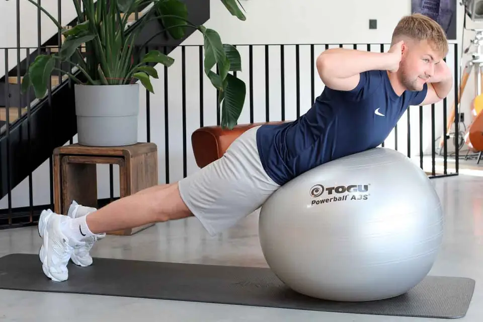Mann führt eine Rückenübung zur Stärkung der Rückenmuskulatur auf einem Gymnastikball aus.