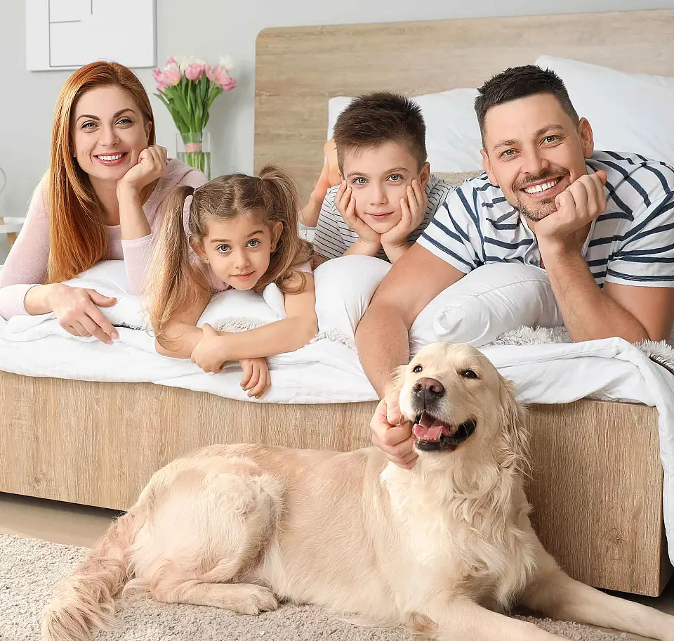 Eltern mit zwei Kindern und Hund liegen auf einem Bett und lächeln in die Kamera